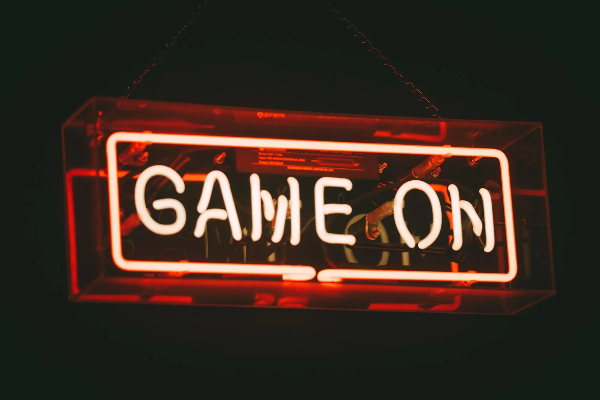Image of a red and pink neon sign saying Game On, against a black background. The words are a surrounded by a neon square boxing them in