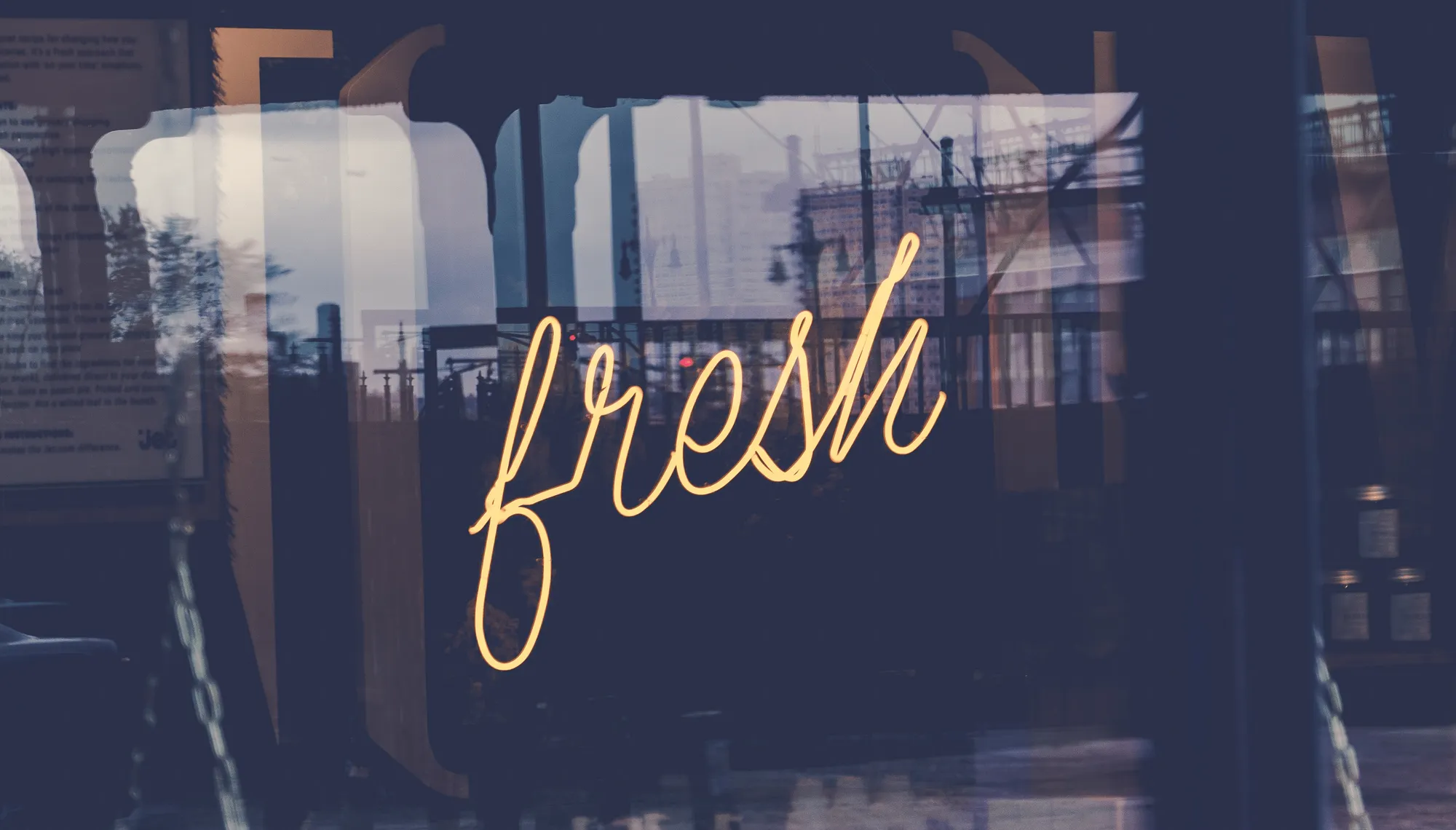 Image of a yellow neon sign in a window saying the word Fresh
